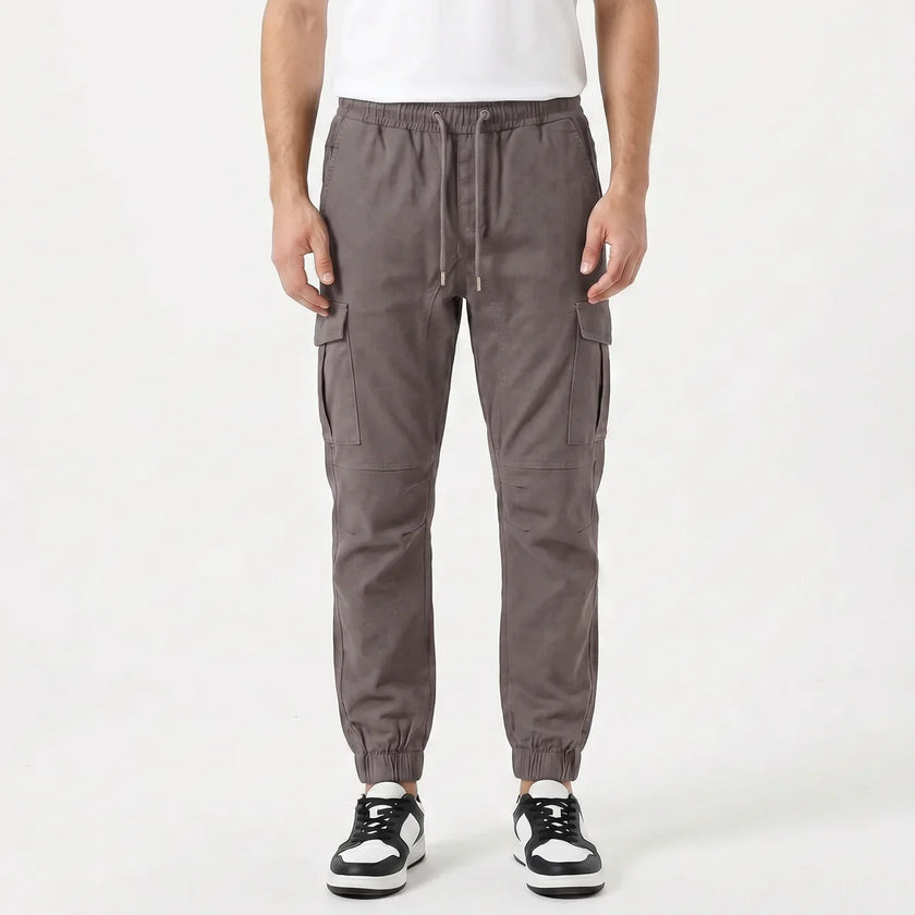Men's slim fit cotton cargo trousers by FJØRNA, featuring multiple cargo pockets and a tailored fit in a neutral color.