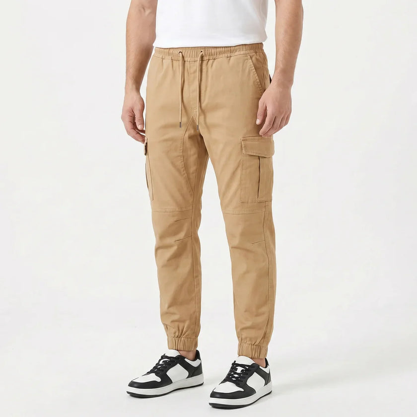 Men's slim fit cotton cargo trousers by FJØRNA, featuring multiple pockets and a sleek, modern design in neutral fabric.