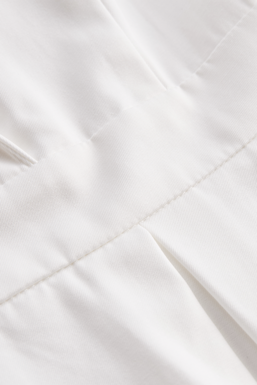 White FJØRNA pleated mini shirt dress, featuring a classic collar, button front, and short sleeves, styled with a fitted waist.