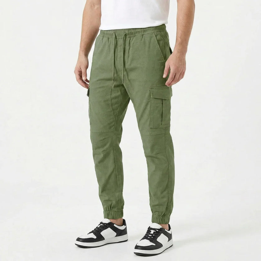 Men's slim fit FJØRNA cotton cargo trousers, shown in a neutral color, with multiple pockets and a tailored fit.