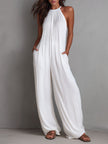 White pleated halter neck wide-leg resort jumpsuit by FJØRNA, featuring flowing fabric and stylish design, shown on a model.