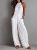 White pleated halter neck wide-leg resort jumpsuit by FJØRNA, featuring flowing fabric and stylish design, shown on a model.