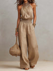 FJØRNA tan cotton linen sleeveless jumpsuit with halter neck, smocked waist, and wide-leg design, perfect for casual summer wear.