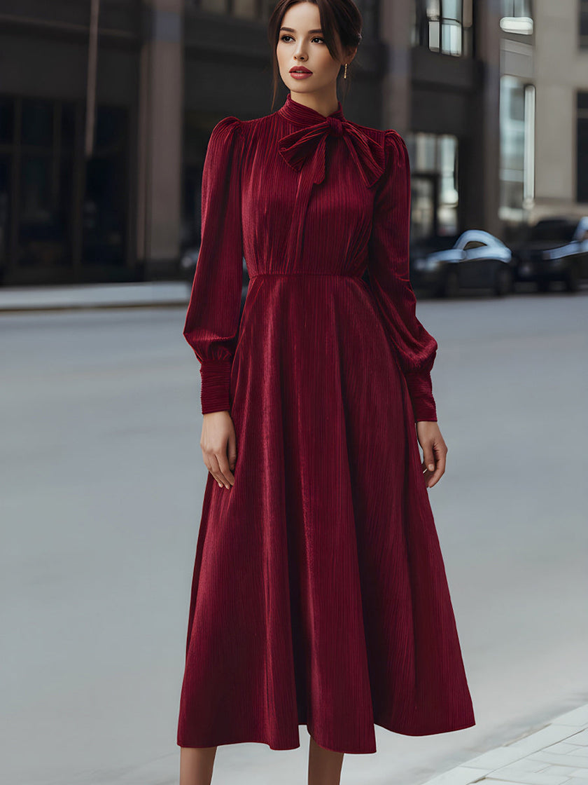 FJØRNA velvet pleated bow-neck midi dress with a fitted waist and elegant pleats, perfect for formal occasions.
