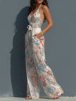 White floral satin halter neck jumpsuit by FJØRNA with wrap front and wide-leg design, shown on a model.