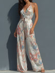 White floral satin halter neck jumpsuit with wrap front and wide-leg design by FJØRNA, featuring a stylish and elegant silhouette.