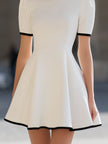 White contrast trim high neck short sleeve flared A-line mini dress by FJØRNA, shown from the front on a model.