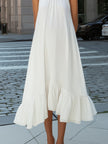 FJØRNA sleeveless pleated halter neck flowing asymmetric midi dress displayed on a model in a stylish outdoor setting.