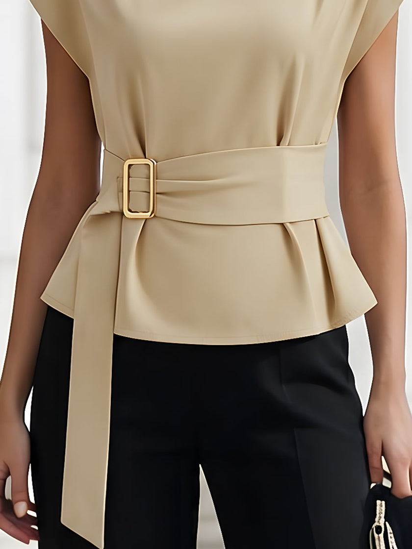 Beige sleeveless women's top by FJØRNA with high neck, tie waist, and gold belt buckle, shown on a model.