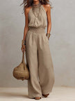 Tan cotton linen sleeveless jumpsuit by FJØRNA with halter neck, smocked waist, and wide-leg design.