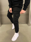 FJØRNA black cargo jogger trousers with multiple pockets and relaxed fit, shown on a model in a casual urban setting.