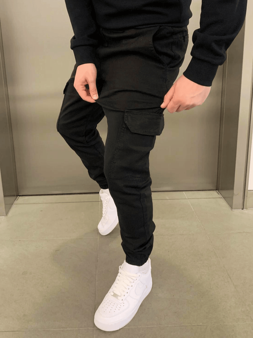 FJØRNA black cargo jogger trousers with multiple pockets and relaxed fit, shown on a model in a casual urban setting.