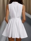 White pleated mini shirt dress by FJØRNA, featuring a collared neckline, long sleeves, and a relaxed fit with pleated skirt detail.