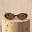 FJØRNA retro oval unisex sunglasses with black frames and tinted lenses, perfect accessories for women.
