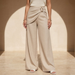 Women’s beige asymmetric waist trousers with metal buckle from FJØRNA, featuring stylish design and comfortable fit.