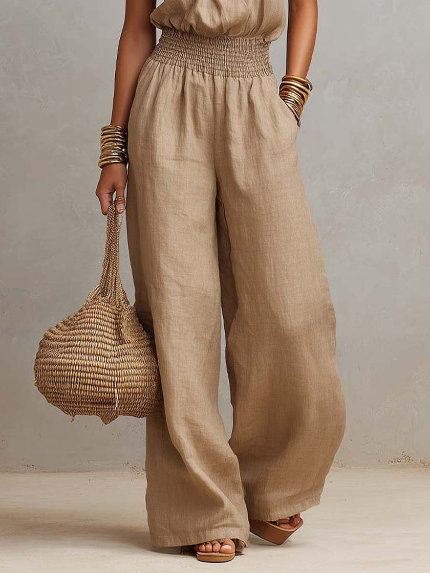 FJØRNA tan cotton linen sleeveless jumpsuit with halter neck, smocked waist, and wide-leg design displayed in the image.