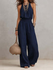 FJØRNA tan cotton linen sleeveless halter neck jumpsuit with smocked waist and wide-leg design, perfect for warm weather.