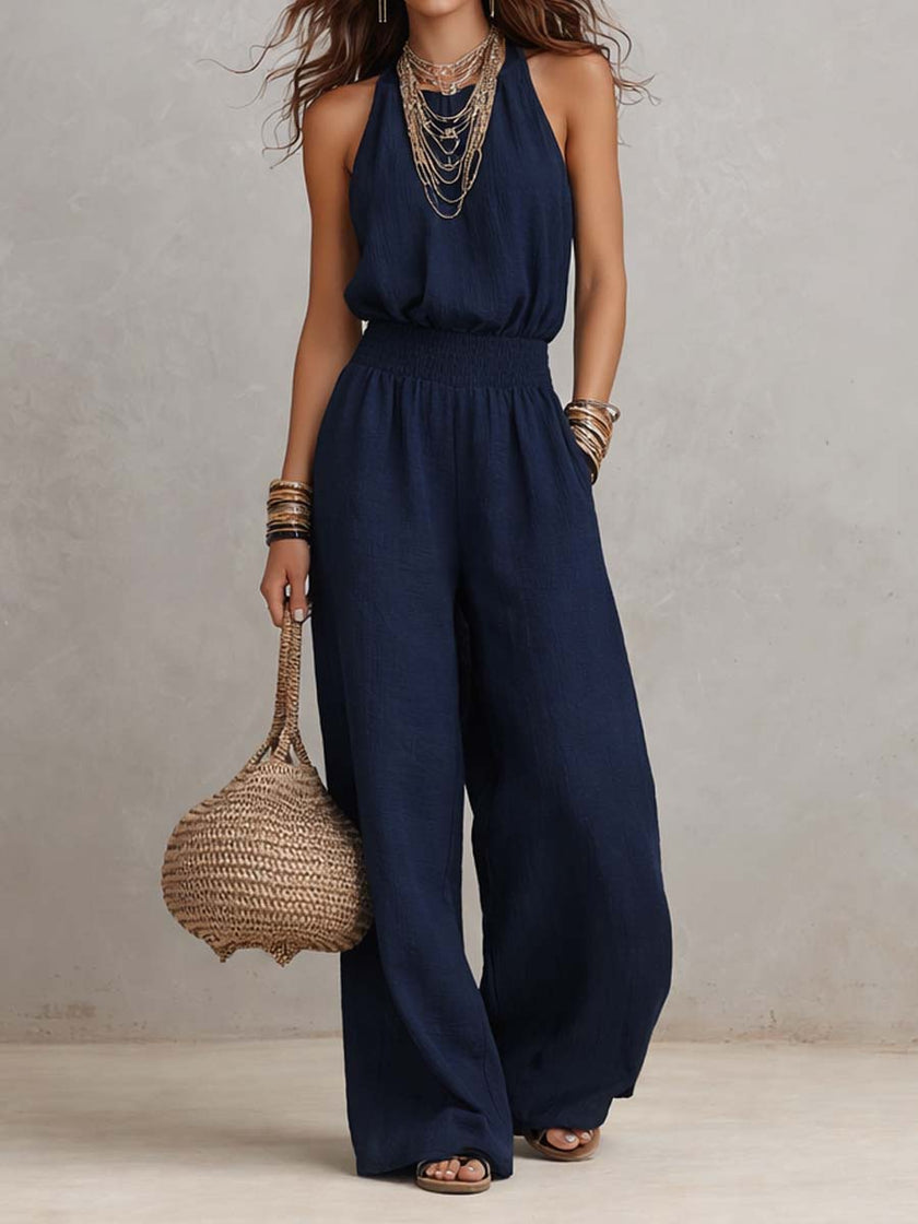 FJØRNA tan cotton linen sleeveless halter neck jumpsuit with smocked waist and wide-leg design, perfect for warm weather.