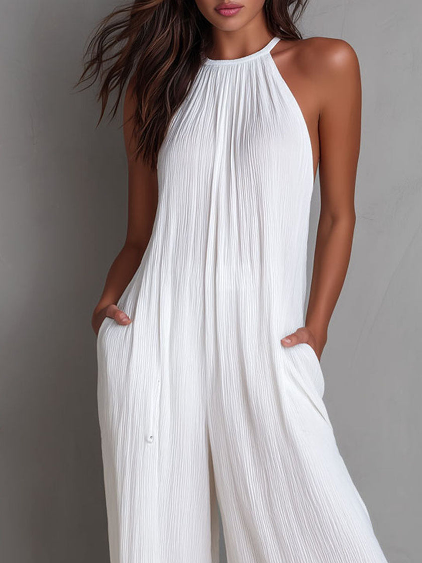 White pleated halter neck wide-leg resort jumpsuit by FJØRNA, featuring flowing fabric and stylish design, displayed on a hanger.