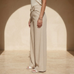 Women’s beige asymmetric waist trousers with metal buckle, stylish FJØRNA pants featuring a modern design and tailored fit.