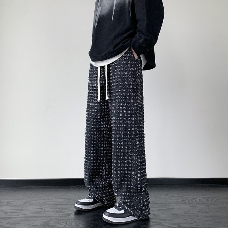 Black distressed trousers by FJØRNA featuring ripped details and a relaxed fit, styled on a model.