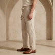 FJØRNA men's linen trousers with drawstring waist, relaxed fit, lightweight breathable fabric, shown on a model.