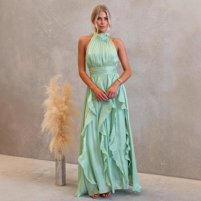FJØRNA elegant women's maxi dress with halter neck and ruffle details, flowing fabric perfect for formal or summer occasions.