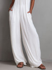 White pleated halter neck wide-leg resort jumpsuit by FJØRNA, featuring a stylish halter top and flowing wide-leg design.