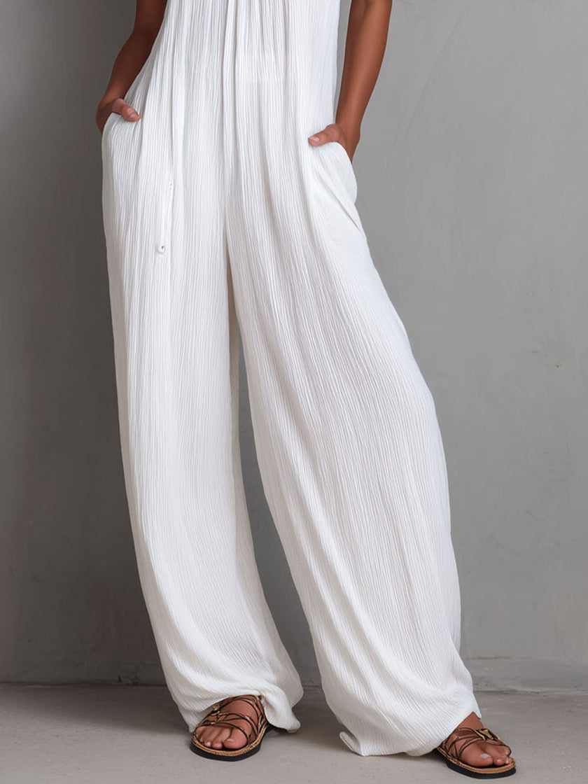 White pleated halter neck wide-leg resort jumpsuit by FJØRNA, featuring a stylish halter top and flowing wide-leg design.