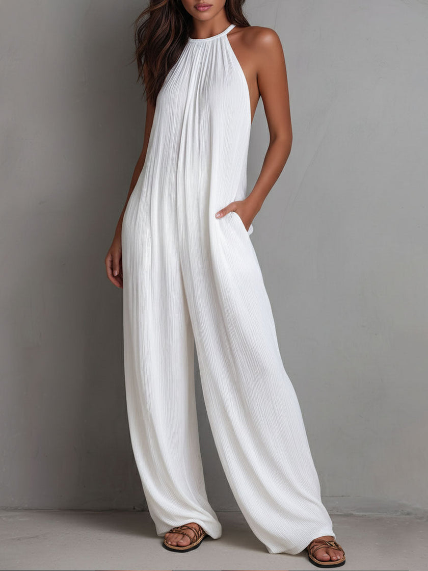 White pleated halter neck resort jumpsuit by FJØRNA featuring wide-leg design and elegant pleats, perfect for warm-weather wear.