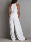 White pleated halter neck wide-leg resort jumpsuit by FJØRNA, featuring flowing fabric and stylish halter design.