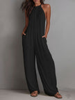 FJØRNA white pleated halter neck wide-leg resort jumpsuit displayed on a model, showing the flowing fabric and stylish design.
