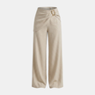 Women’s beige asymmetric waist trousers by FJØRNA featuring a metal buckle and tailored fit, displayed on a clean background.