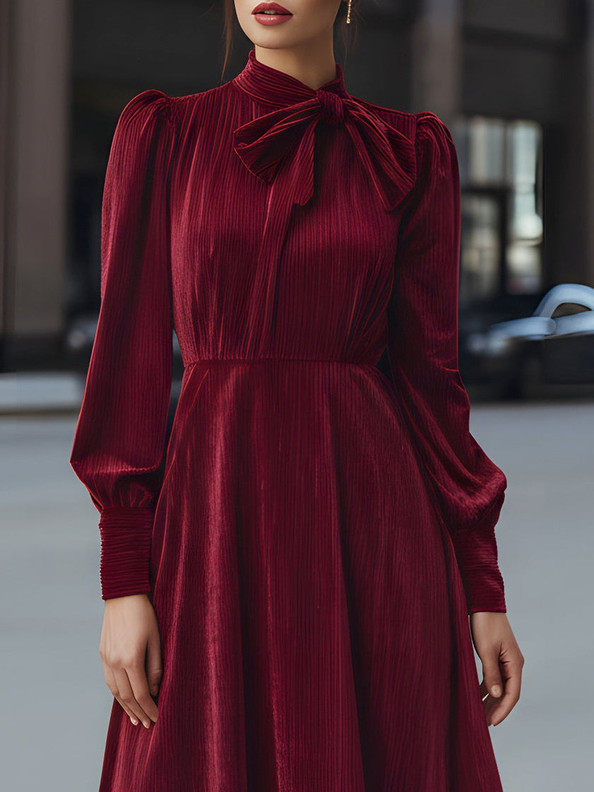 FJØRNA velvet pleated bow-neck midi dress displayed on a hanger with elegant pleats and a bow detail at the neckline.