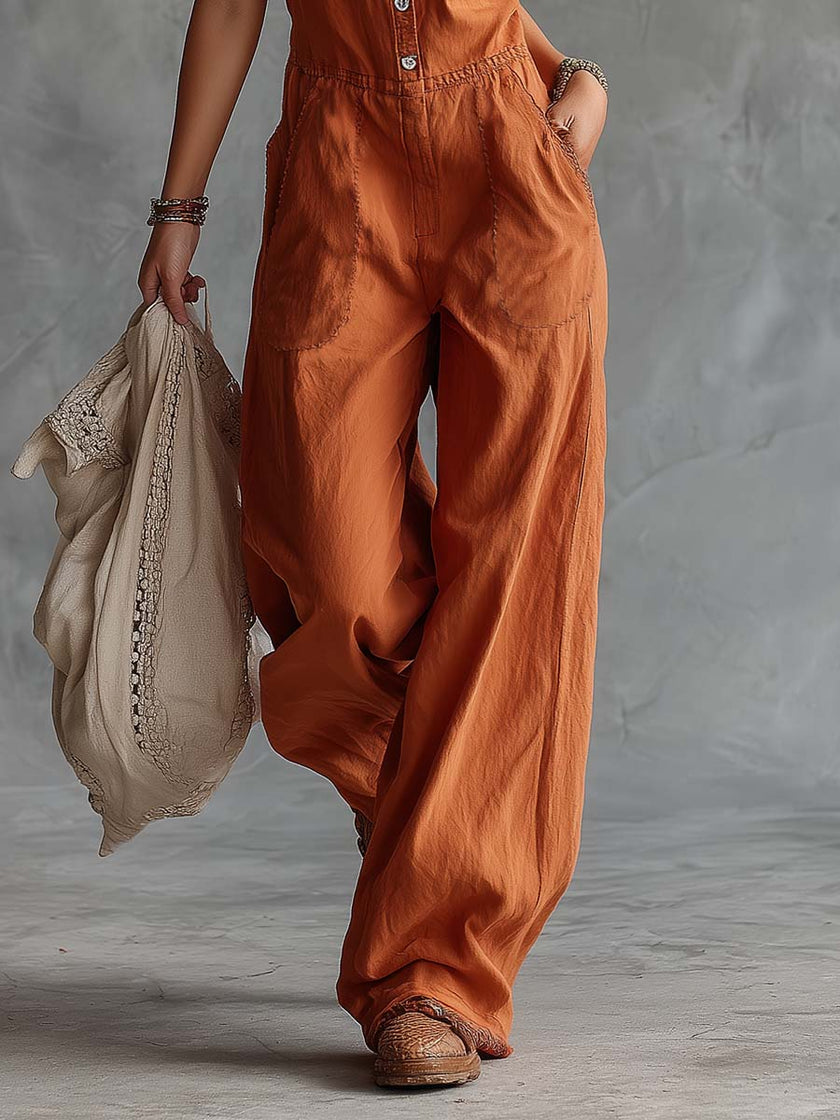 Rust orange FJØRNA cotton sleeveless Western V-neck jumpsuit hanging on a hanger with a belt at the waist.
