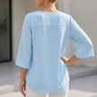 Back view of FJØRNA women's flowing V-neck blouse with curved hem and slit sleeves, showcasing lightweight, elegant fabric.