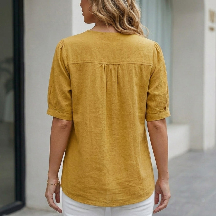FJØRNA women's summer linen blouse with short sleeves and front pockets, shown from the back. Light, breathable fabric.