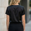 FJØRNA women's summer blouse with V-neck, short satin sleeves, casual style, shown from the back in a natural setting.