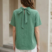 FJØRNA women's summer blouse with high neck and short sleeves, shown from the back in a light, breathable fabric.
