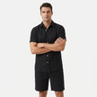 FJØRNA men's black linen two-piece set with buttoned short sleeve shirt and matching shorts, model crossing arms.