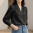 Black women's summer blouse with V-neck, puff sleeves, and pleated design from FJØRNA, displayed on a hanger.