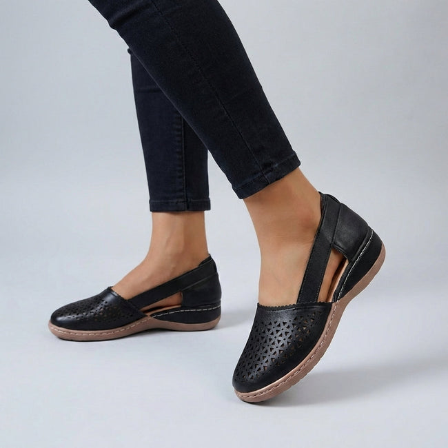 Black FJØRNA orthopedic wedge sandals with scalloped trim and side cut-outs, showing the stylish design and comfortable sole.