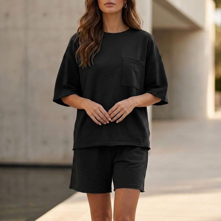 Black FJØRNA oversized two-piece relaxed set with chest pocket and wide-leg shorts, worn by a model standing outdoors.