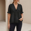 Black women's relaxed peplum blouse by FJØRNA with ruffled V-neck and tiered hem, shown on a hanger against a white background.