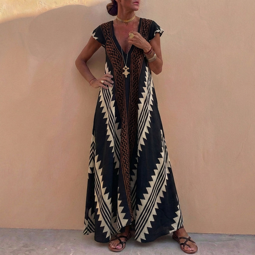 Black FJØRNA bohemian-inspired flowing A-line maxi dress with deep V-neck and geometric motifs, showcasing a relaxed, elegant style.