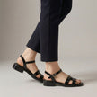 Black FJØRNA ankle-length flat sandals with ankle strap and buckle, featuring a sleek design and comfortable fit.