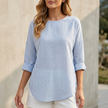 Blue FJØRNA relaxed-fit women's blouse with rolled sleeves and curved hem, shown on a model.