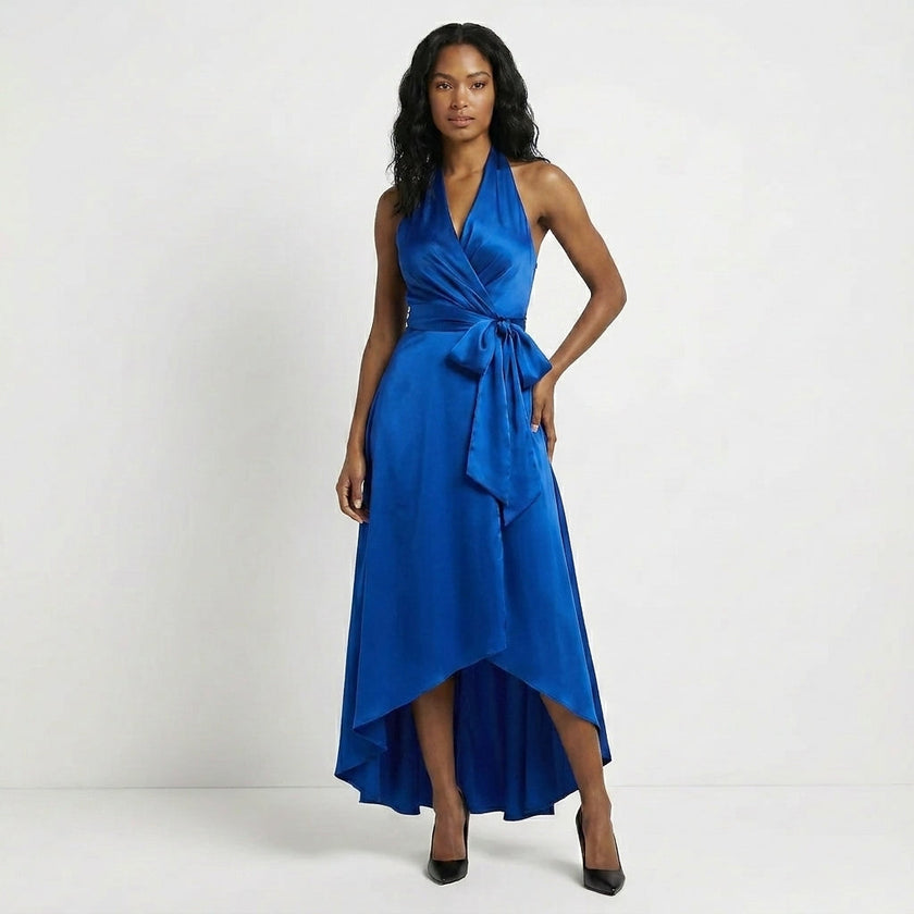 Blue satin FJØRNA maxi dress with halter neck, bow tie waist, and ruffled hem, showcasing elegant and flowing design.