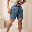 FJØRNA Jess men's quick-dry relaxed-fit swim shorts in blue with side pockets and slit hem, suitable for beach or poolside wear.