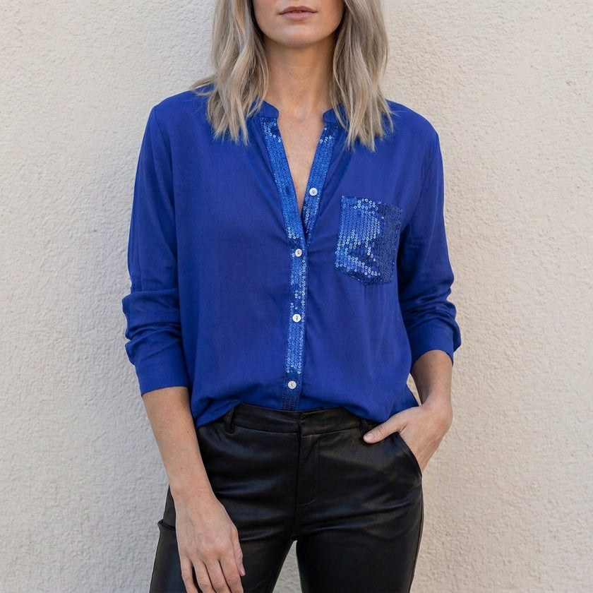 Blue denim summer blouse for women with V-neck and button front from FJØRNA, displayed on a hanger.